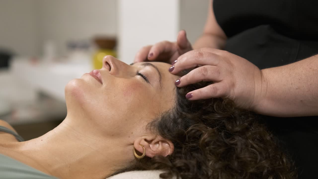 Esteticista realizando un masaje relajante en las sienes a una mujer recostada con los ojos cerrados.