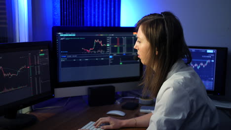 Female-stock-trader-wearing-headset-and-microphone-making-trades-on-the-market-looking-at-graphs-and-talking-to-a-trading-client