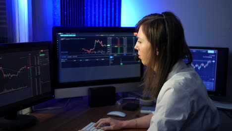 female stock trader wearing headset and microphone making trades on the market looking at graphs and talking to a trading client