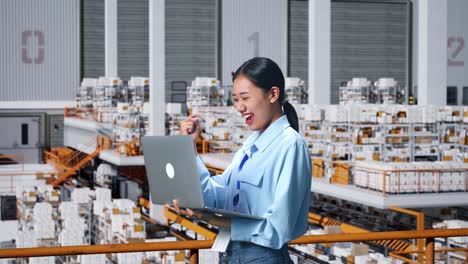 side view of happy asian business woman celebrating using laptop computer in the warehouse