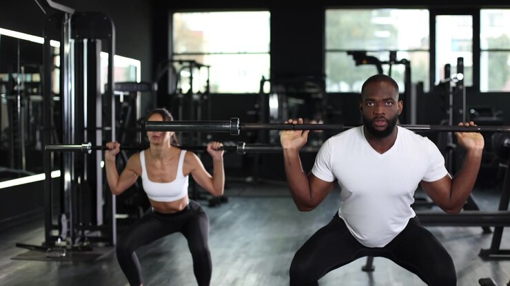 Athletic Man and Woman Performing Barbell Squats in Gym