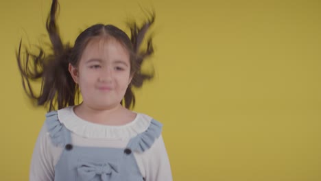 Studio-Portrait-Of-Hyperactive-Girl-Smiling-And-Pulling-Faces-Against-Yellow-Background