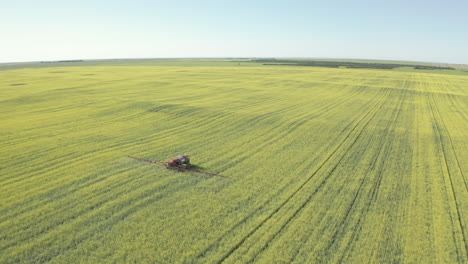 Tractor-Rociando-Cultivos-En-Un-Campo-Verde-Y-Soleado,-Rastreando-Disparos-De-Drones