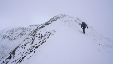 Hiker-walking-over-mountain-ridges-and-snow-in-winter-time-on-a-foggy-day