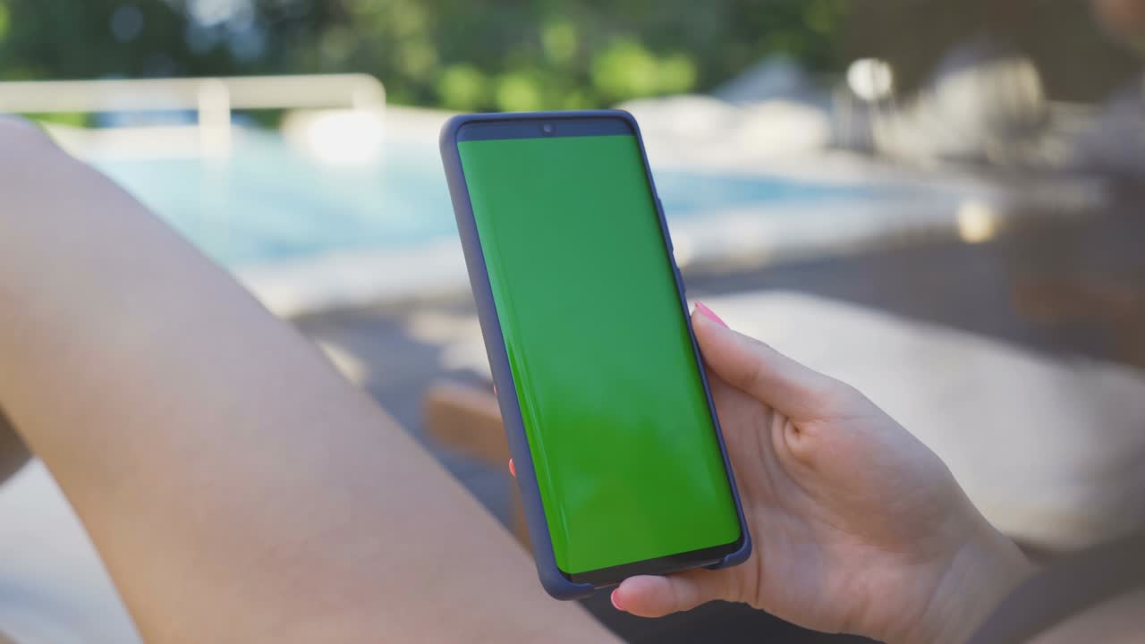 Mano di donna che usa lo smartphone con schermo verde in piscina all'aperto.