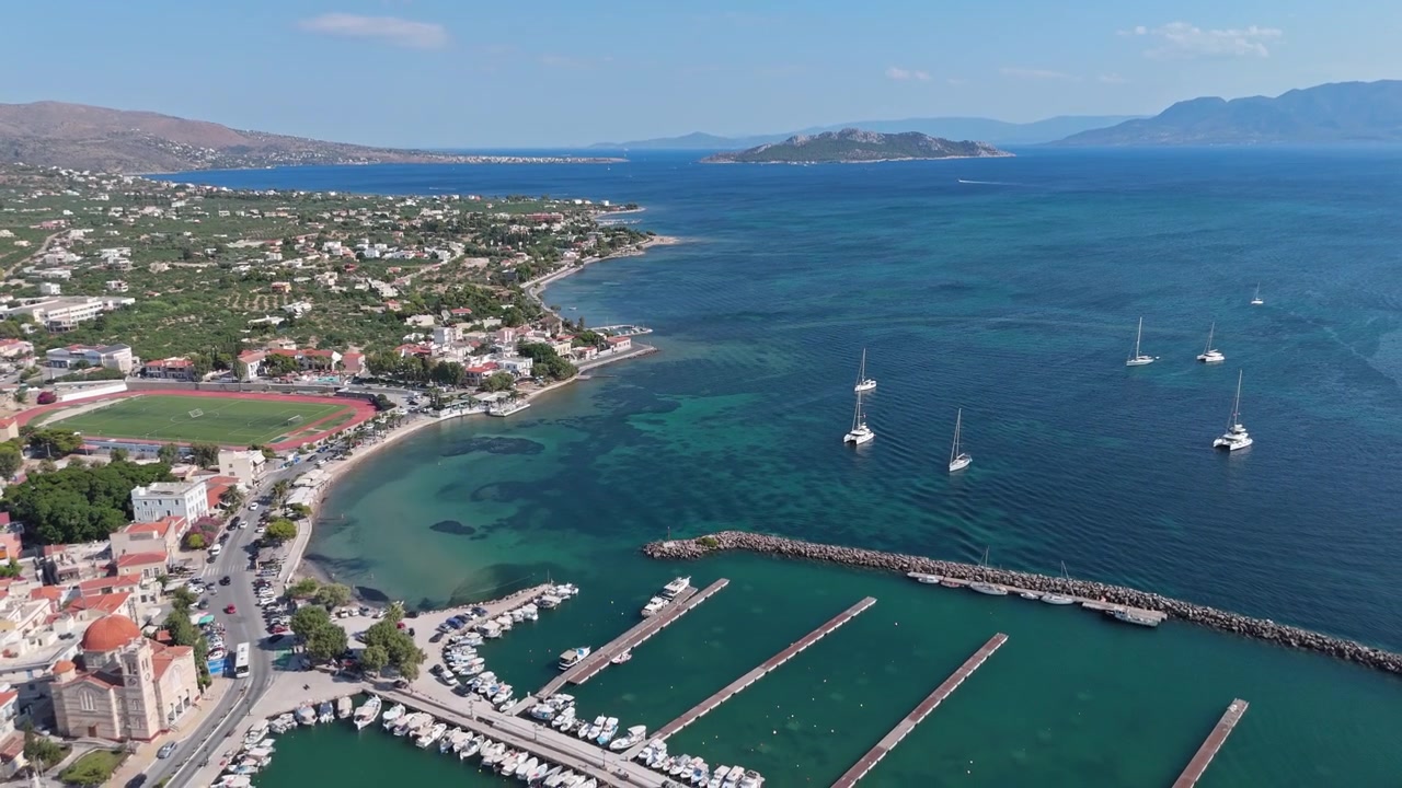 Città costiera di Egina con moli del porto turistico, barche a vela ancorate e baie turchesi poco profonde lungo il Golfo Saronico.