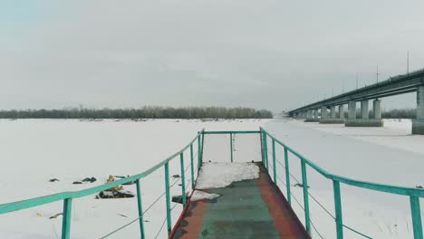 old rusty pier with snow and ice at white frozen river