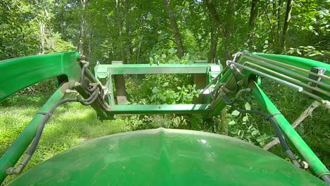 pov of equipment operator using a loader with forks to push a small pile of tree limbs in a clearing in the woods