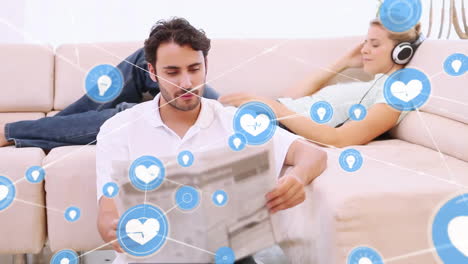 Animation-of-network-of-connections-with-icons-over-caucasian-couple-sitting-on-sofa