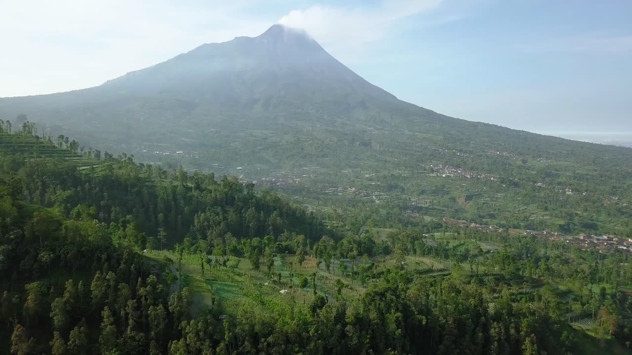 Reversing drone shot of Merapi volcano with rural view of vegetable plantation and dense of trees in slightly foggy weather. 4K aerial view of plantation with rural view Central Java, Indonesia