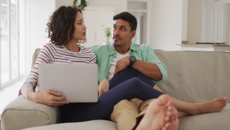 Hispanic-couple-sitting-on-sofa-looking-at-laptop-discussing