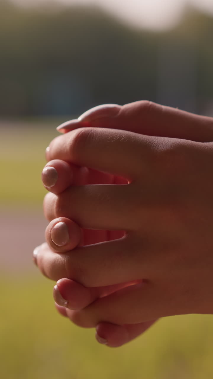 primer plano de individuos que se juntan las manos en una postura relajada y reflexiva contra el fondo borroso de un paisaje verde exuberante y árboles lejanos