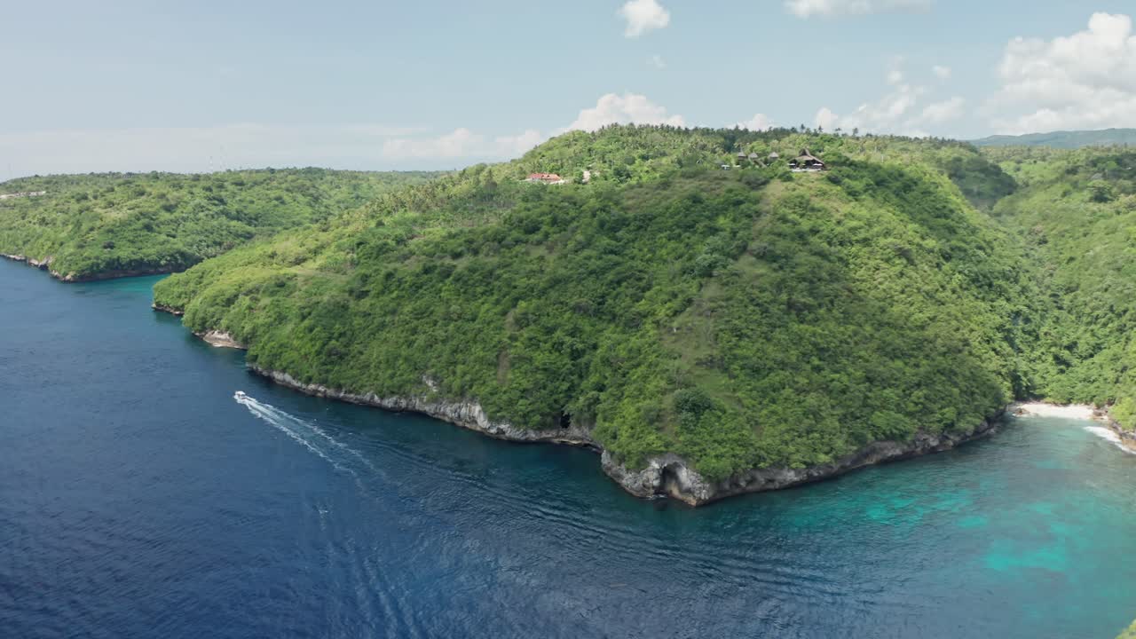 A sweeping aerial shot of the undeveloped, lush hilly coastline of Nusa Penida, Bali, Indonesia, showcasing the dense tropical greenery covering the undulating landscape