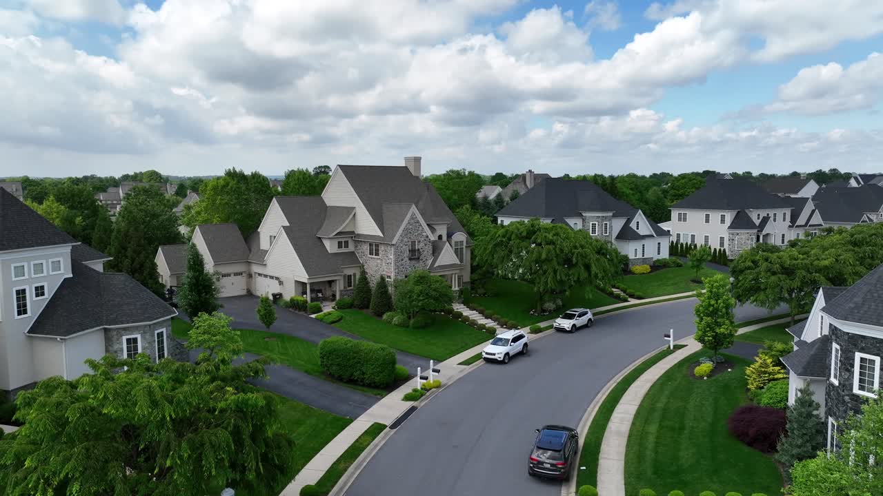 Parking cars on street in luxury neighborhood with large single Family homes. Puffy clouds at sky in sporing season. Historic style of architecture houses. Aerial rising wide shot.