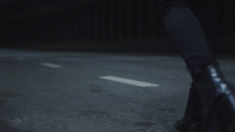 Female-legs-walking-highway-in-black-shoes-or-dark-road-with-passing-cars.