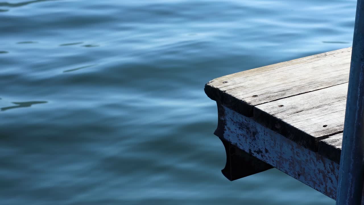Wooden dock gently sways above tranquil blue water