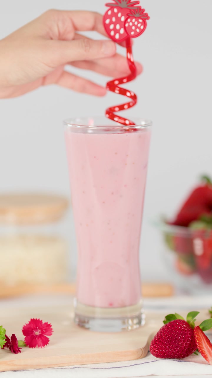 Una mano inserisce una cannuccia rossa a spirale in un cremoso milkshake alla fragola, illuminazione brillante da studio, vista ravvicinata.