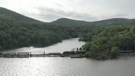 Toma-De-Drone-De-Un-Largo-Tren-De-Carga,-Volando-Hacia-La-Izquierda-Y-Siguiendo-Al-Tren,-Con-Un-Puente-Al-Fondo.