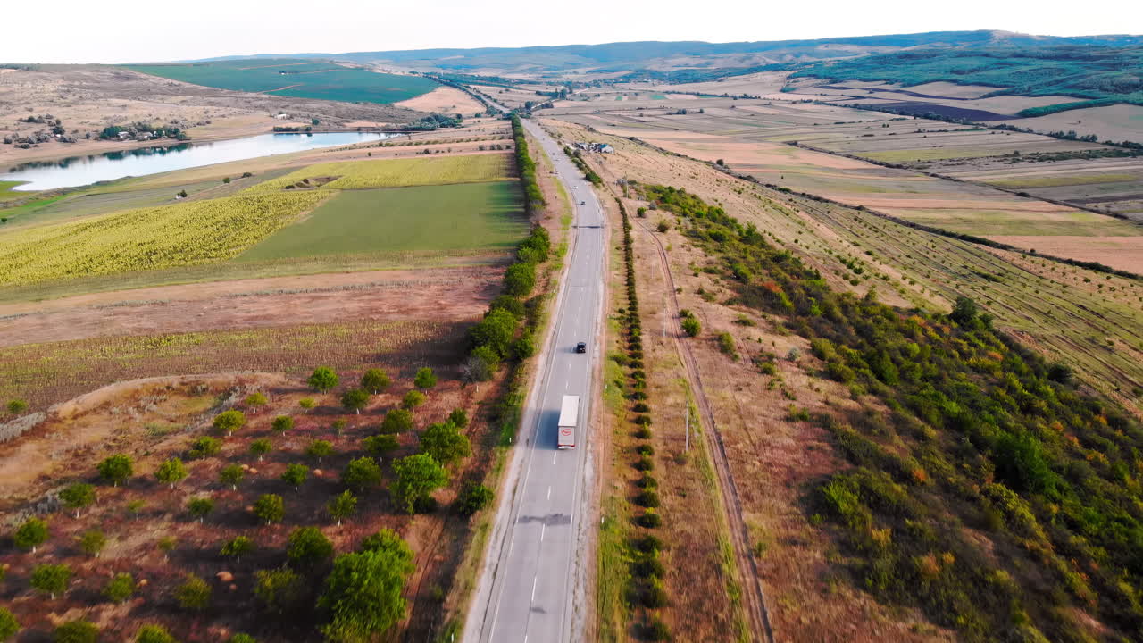 Visão aérea de drone de uma estrada com carros em movimento nas montanhas. Pequena vila e colinas verdes ao fundo. Dia ensolarado. Balti, Moldávia
