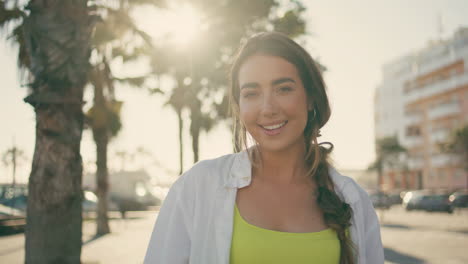 modelo sonriente posando cámara en las palmeras callejón retrato. mujer relajándose en la ciudad