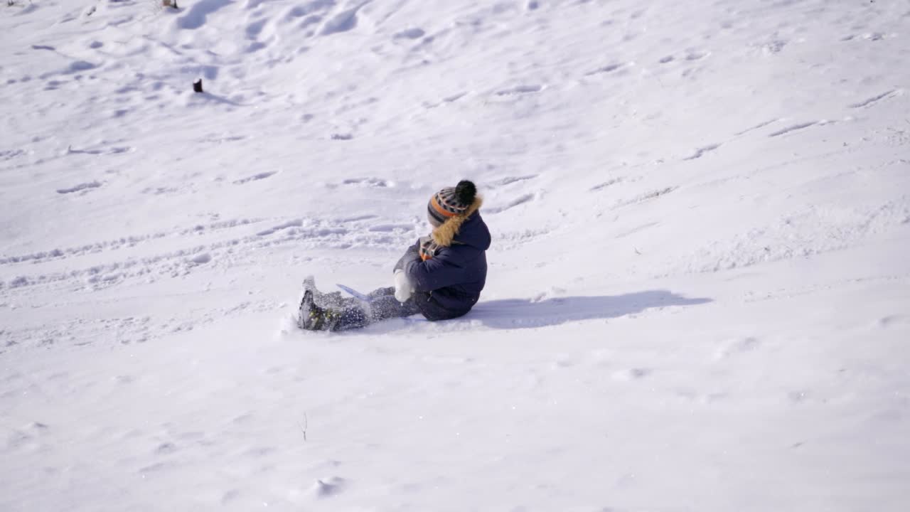Little boy sledging in winter. Happy child riding down from a snowy slide outdoors. Winter games and fun. Slow motion.