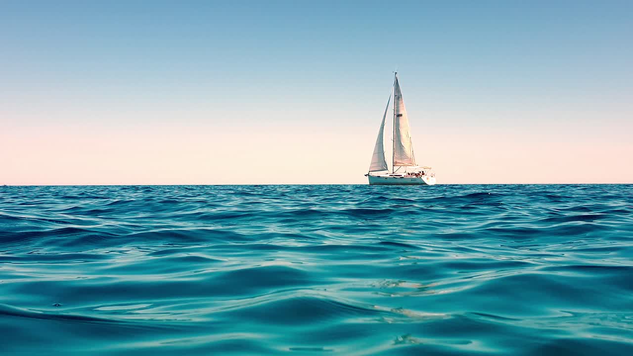 vista de ángulo bajo de un pequeño yate blanco navegando lentamente en el mar abierto y tranquilo