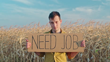 man holding sign "need job" in a cornfield