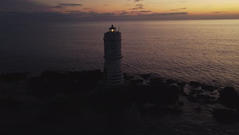 Drone-Aéreo-Volando-Hacia-El-Faro-En-Alta-Mar-En-Rocas-En-Calasetta,-Atardecer