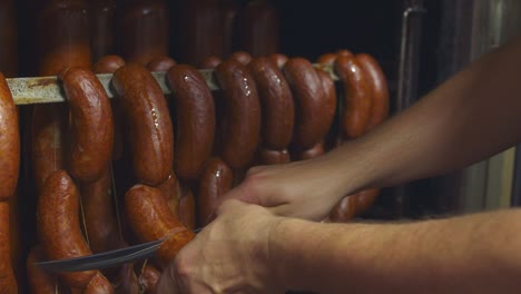 the butcher cuts a fresh piece of sausage production from the smokehouse. close up