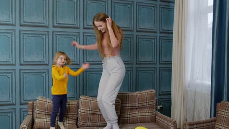 Happy-funny-family-mother-and-child-kid-daughter-dancing,-jumping-on-sofa,-listening-music-at-home