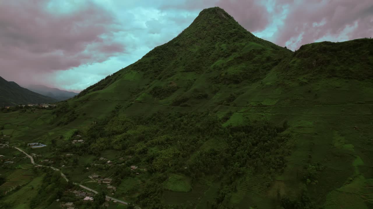 vista panorámica del avión no tripulado: círculo aéreo alrededor de la montaña verde con una carretera de campo pintoresca y un dramático movimiento de nubes naranja