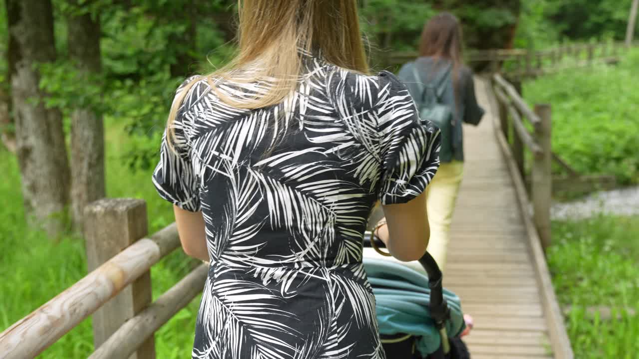 Giovane madre che spinge una carrozzina su un ponte di legno in una foresta verde