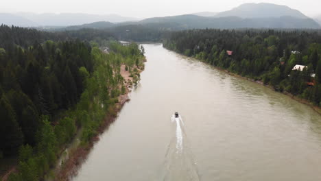 aerial shot following a boat speeding down flathead river, surrounded by pine forest and mountains, covered by smoke from a nearby wildfire