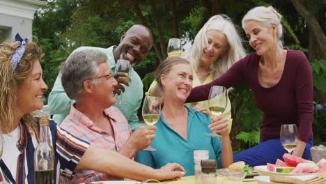 animation of diverse happy senior female and male friends eating lunch in garden