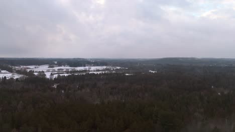 tilting aerial shot of forest landscape and frozen fields in caledon, southern ontario, canada.