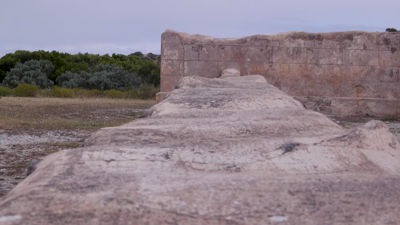 Un muro de piedra desgastado de una estructura antigua, rodeado de naturaleza. Ideal para documentales históricos y contenido de viajes