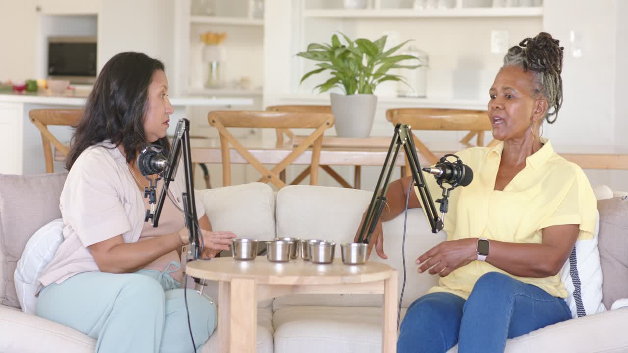 Donne anziane afroamericane e asiatiche a casa, con l'ospite a sinistra che inizia la discussione, prendendo una tazza vicino ai microfoni.