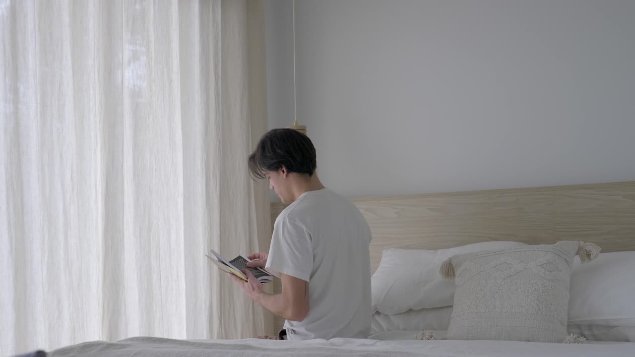 남자가 침대의 가장자리에 앉아 책을 읽습니다.