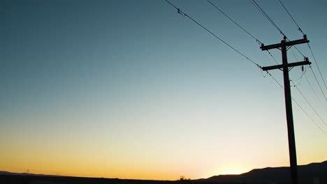 a serene sunset over mountains with power lines and road signs, capturing the tranquility of the open landscape at dusk