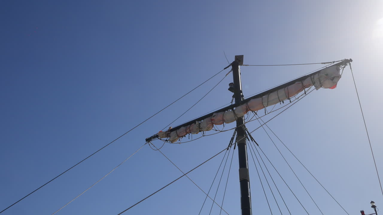 el mástil del barco pirata y las velas enrolladas se encuentran contra un cielo despejado, los rayos de sol proyectando un resplandor, perfectos para temas de aventura y descubrimiento de navegación