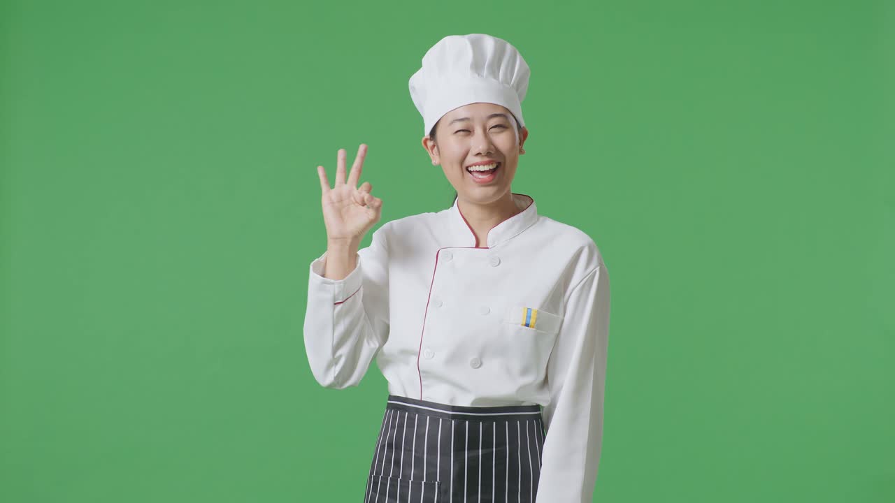 Asian Woman Chef Smiling And Showing Okay Gesture To Camera While Standing In The Green Screen Background Studio