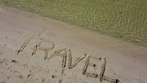 camera tilts down from the horizon showing the sea to travel written in the sand on a beach