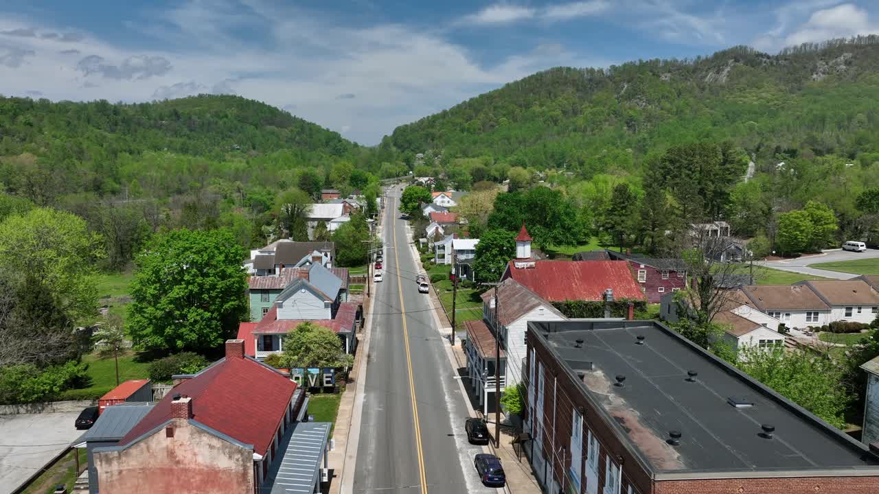 Straight street in small american town with red brick houses and Buildings following between green mountains. Aerial wide shot. Sunny day in spring. Virginia state, USA. Old historic church building
