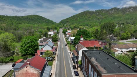 straight street in small american town with red brick houses and buildings following between green mountains. aerial wide shot. sunny day in spring. virginia state, usa. old historic church building