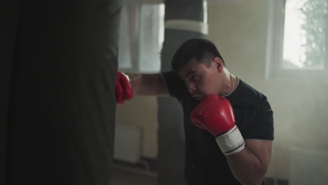 boxer punches stuffed bag blocking face in sports club. trained sportsman hits equipment in boxing gym slow motion. combat techniques performance