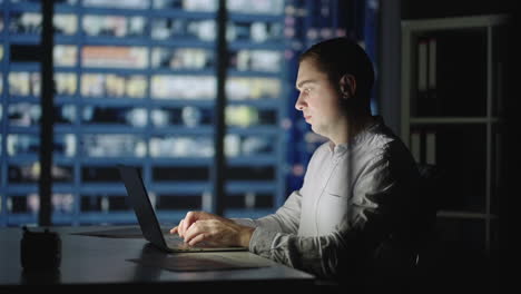 businessman returning to office opening laptop lid and continue in evening work. handsome caucasian man against night city scene in background.