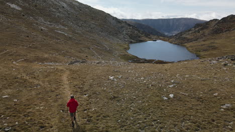 man on a red coat walking on the mountains arriving to a beautiful little lake in puymorens