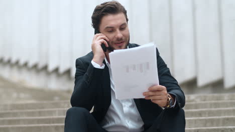 Businessman-talking-with-client-on-smartphone-at-street.-Man-looking-at-graphs