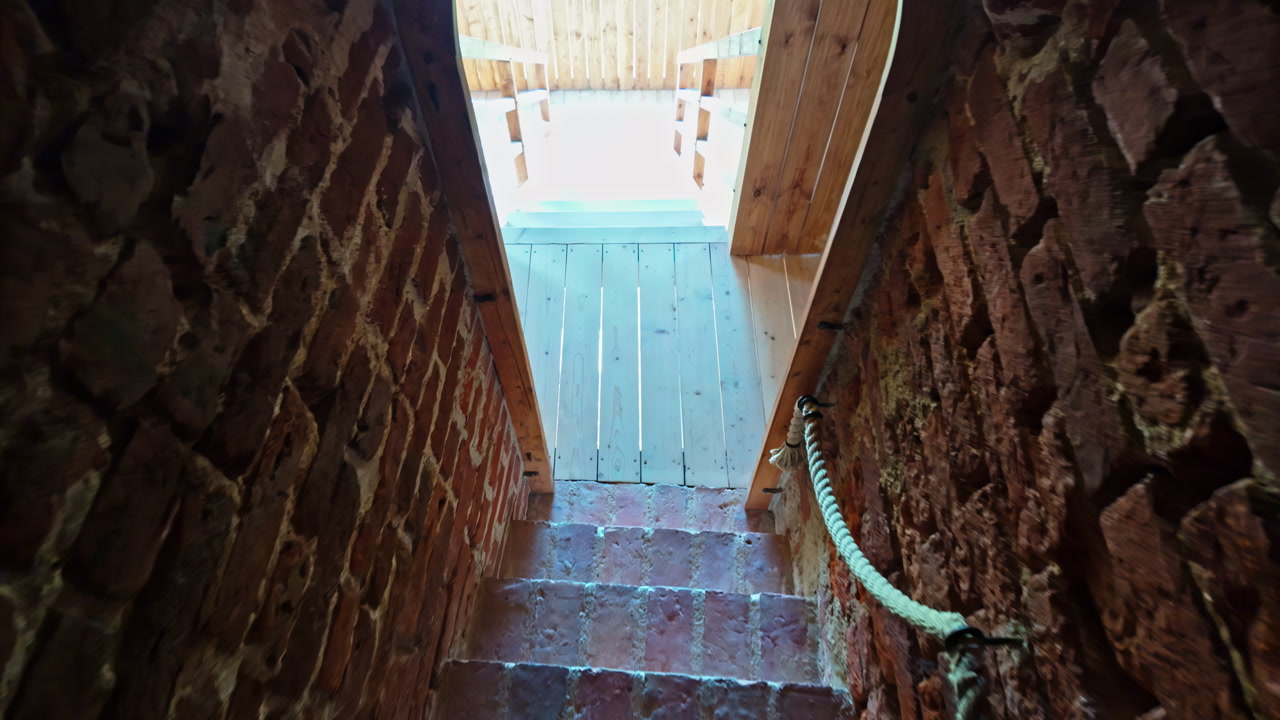 Narrow brick stairway leads upward to a wooden door with daylight at the top, Bauska, Latvia