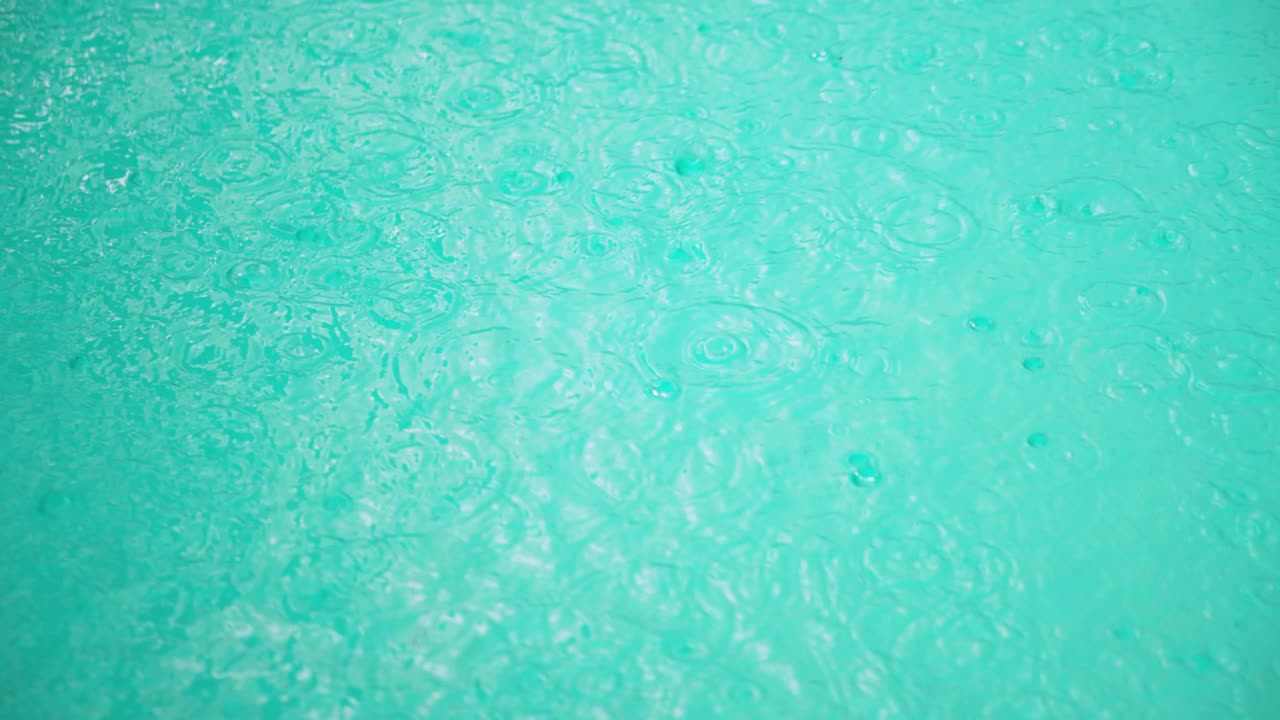 Slow motion top-down shot of turbulent pool surface during medium rain, raindrops creating waves that interfere with each other